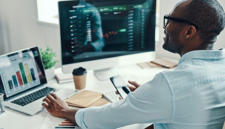 man sits at a laptop and computer with data on the screen
