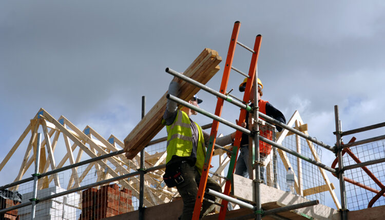 Low view of two construction workers on top of house frame
