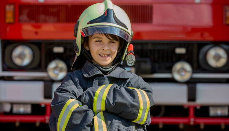 Child dressed in fire fighters cloths in a fire station with fire truck