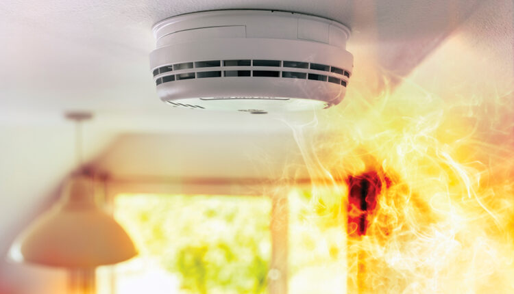 Smoke detector and interlinked fire alarm on ceiling in action background