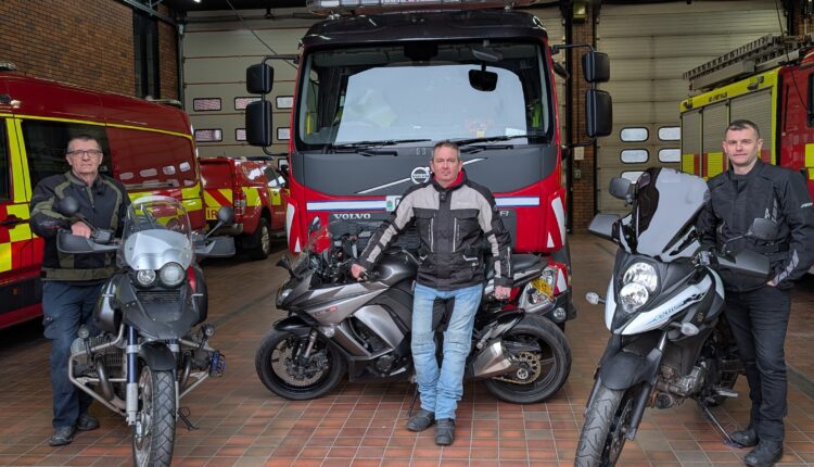 Three fire fighters standing with their motorcycles in front of a fire station