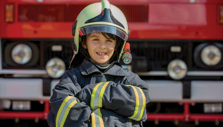 Child dressed in fire fighters clothes in a fire station with fire truck