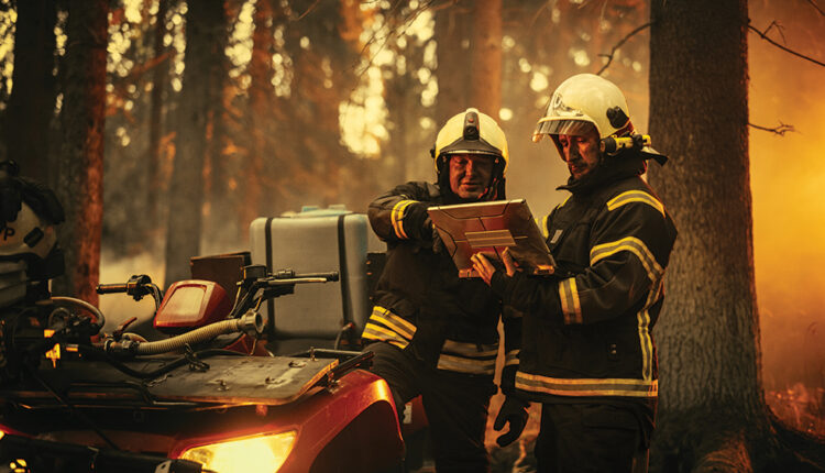 Portrait of Two Professional Firefighters Standing Next to an All-Terrain Vehicle, Using Heavy-Duty Laptop Computer and Figuring Out a Best Strategy for Extinguishing the Wildland Fire